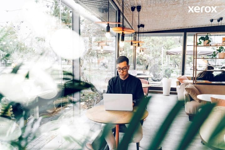 Un homme travaille avec diligence sur son ordinateur portable dans un caf&eacute; anim&eacute;, immerg&eacute; dans ses t&acirc;ches au milieu d'un environnement anim&eacute;.