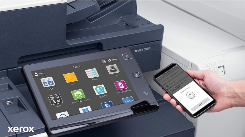 Xerox® ConnectKey® : impression et numérisation mobiles Gros plan de la main d'une personne tenant un smartphone, qui est connecté sans fil au panneau de commande à écran tactile d'une imprimante multifonction Xerox, mettant en valeur les capacités d'impression et de numérisation mobiles transparentes de Xerox ConnectKey.